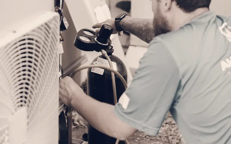 HVAC technician connecting a refrigerant gauge hose to an outdoor air conditioning unit